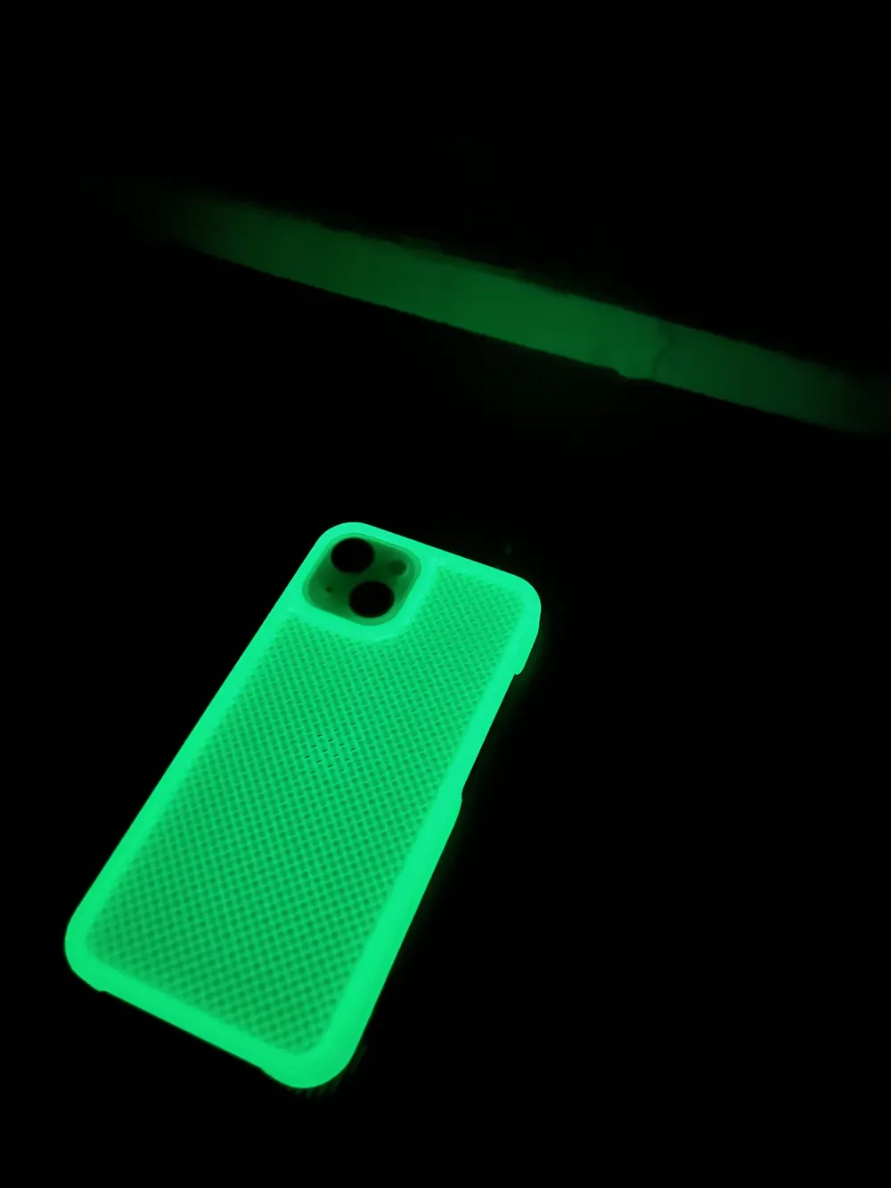 A textured glow in the dark phone case glowing green on a dark surface