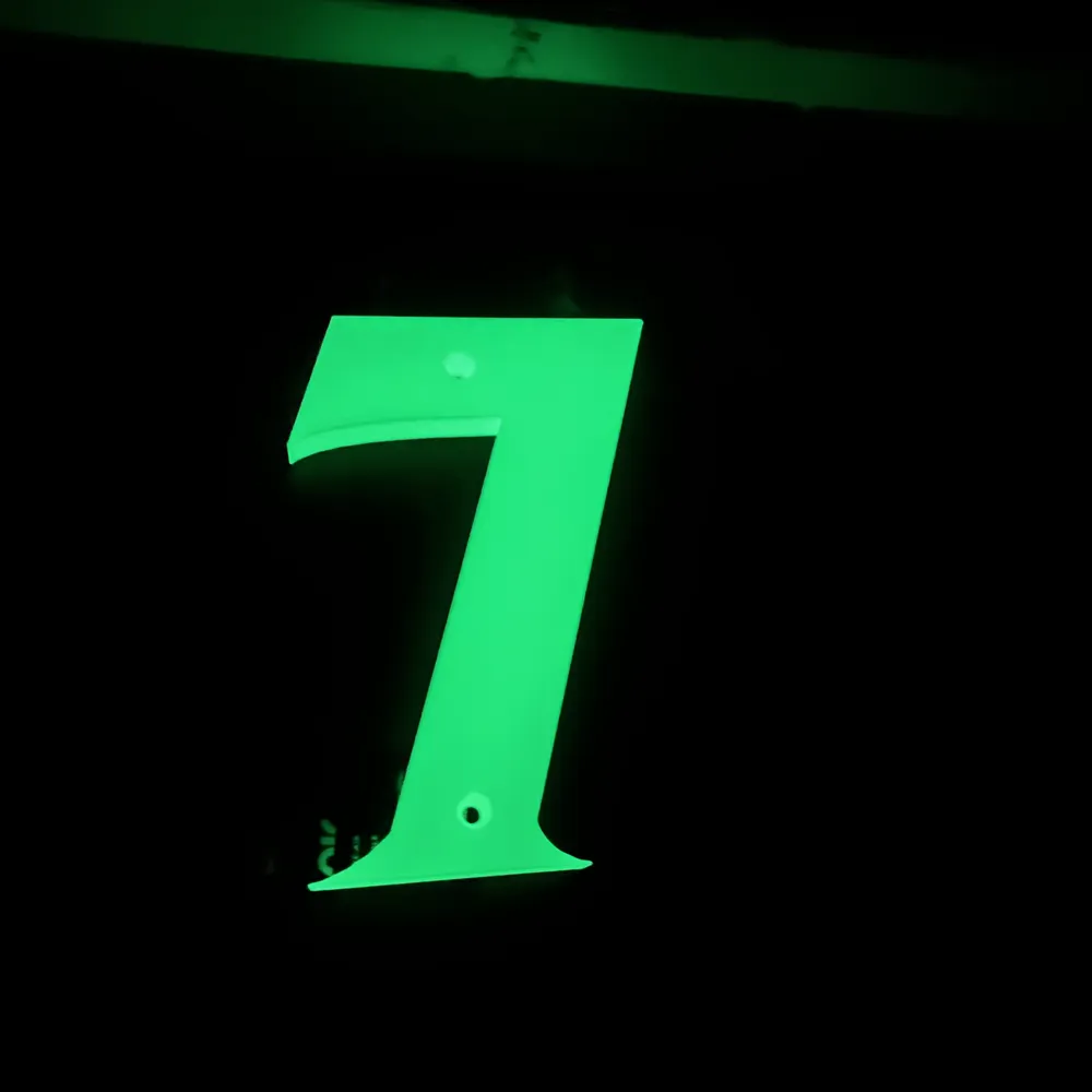 A 3D printed house number seven glowing bright green in complete darkness