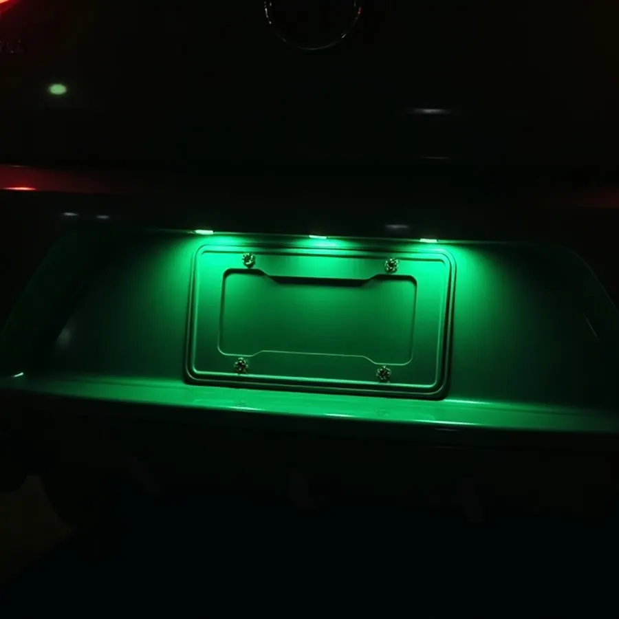 A license plate frame glowing green on the back of a car at night
