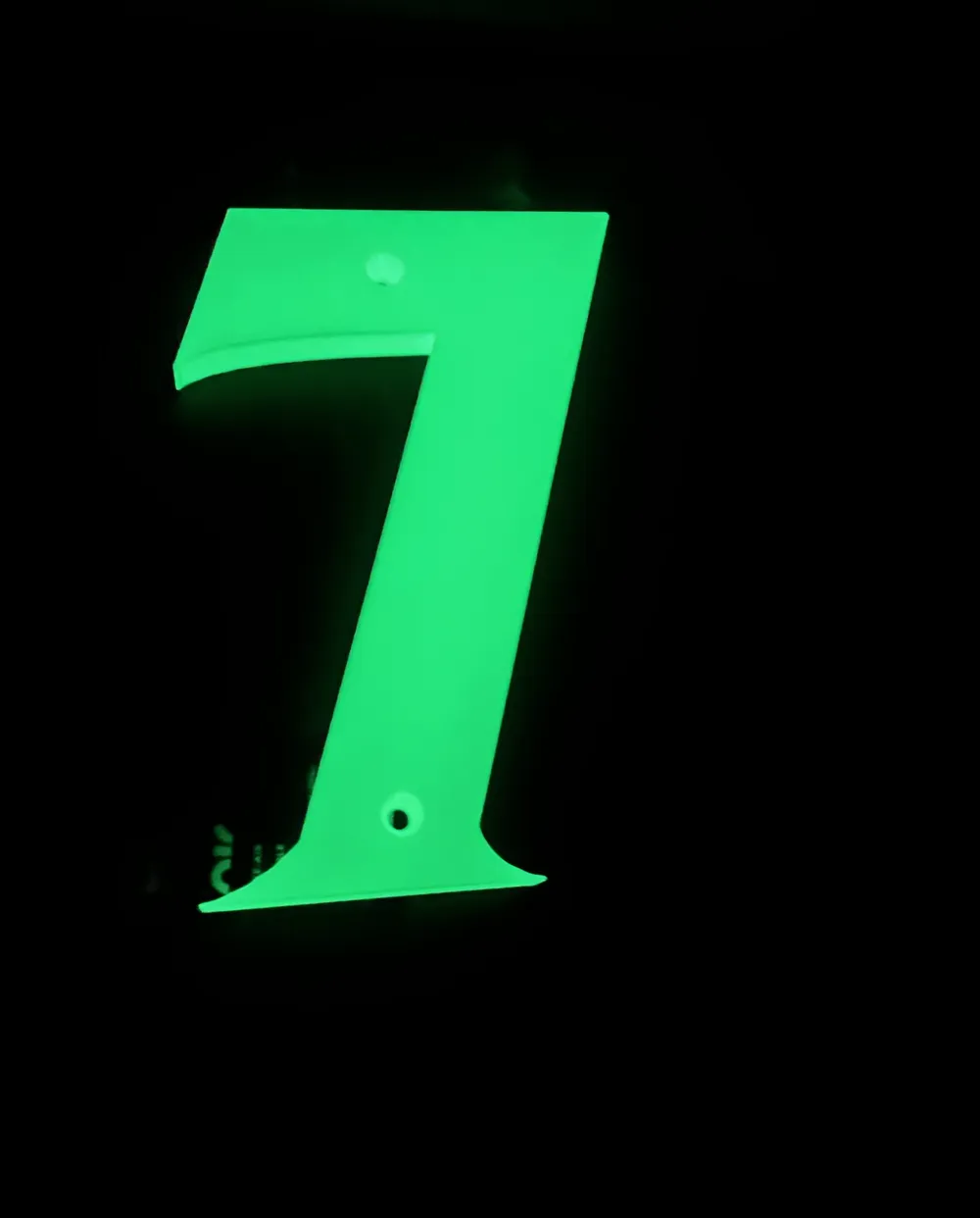 A 3D printed house number seven glowing bright green in a completely dark room